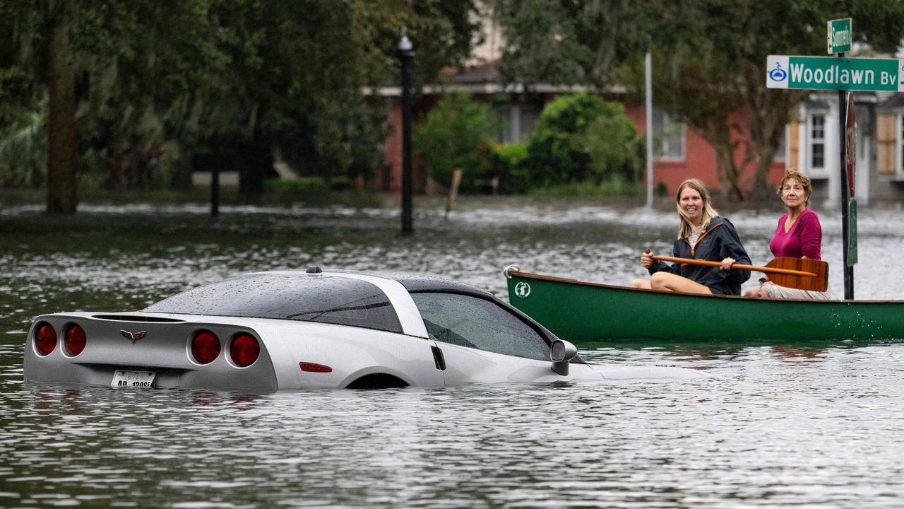 Two women canoe on the streets of Central Florida Orlando.  It's the only way to get around parts of town, as the half-sunken Chevy Corvette shows.